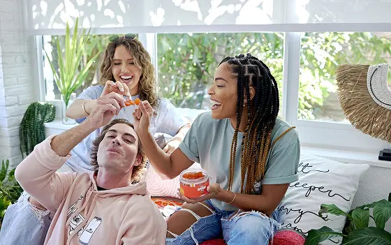 A group of friends relaxing on a bright couch, sharing gumnmies, casual and cozy, indoors with plants and soft cushions